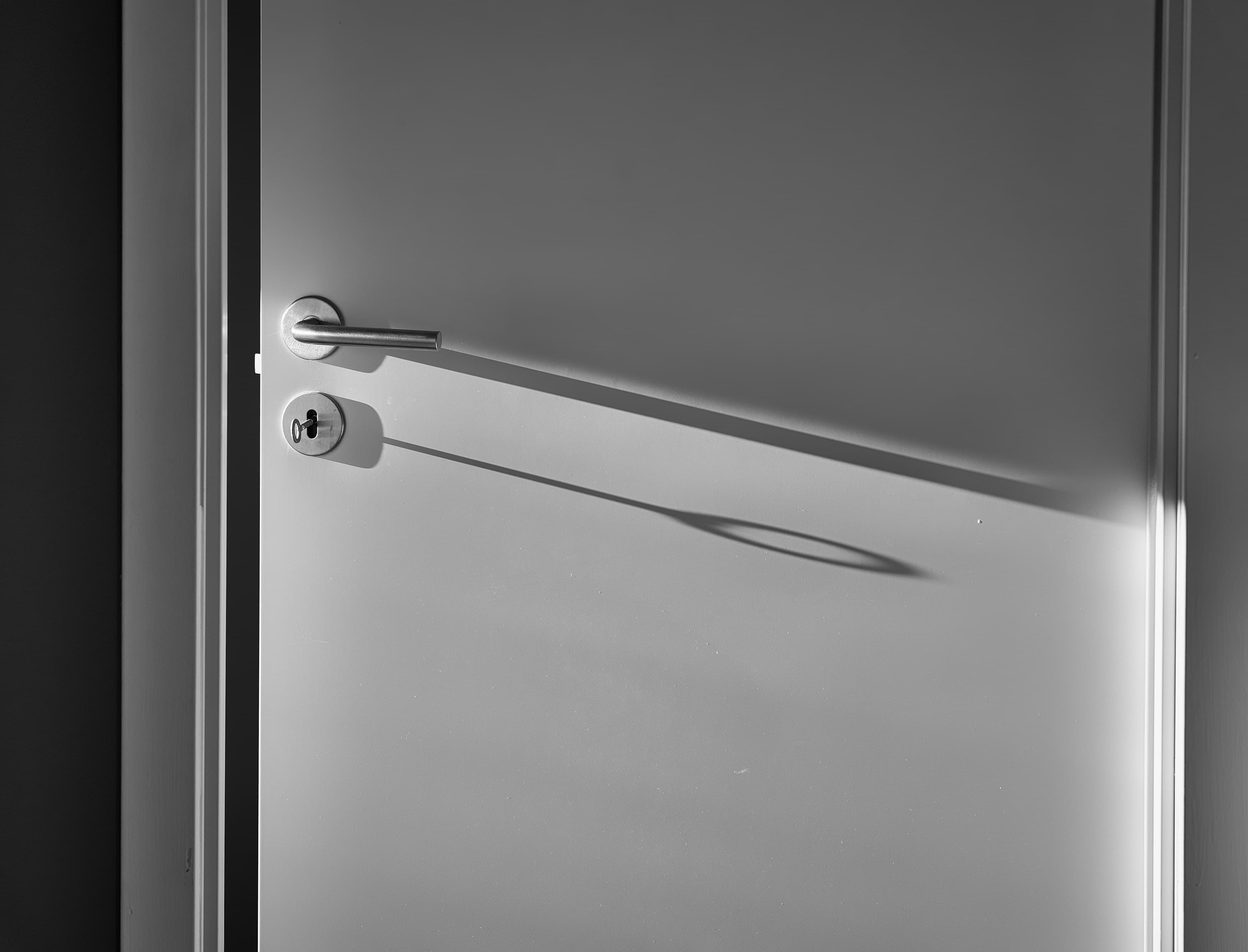 Stainless lever handle casting a long shadow across a white door